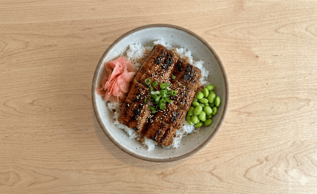 Grilled eel over rice with sesame seeds, green onions, pickled ginger, and edamame beans.